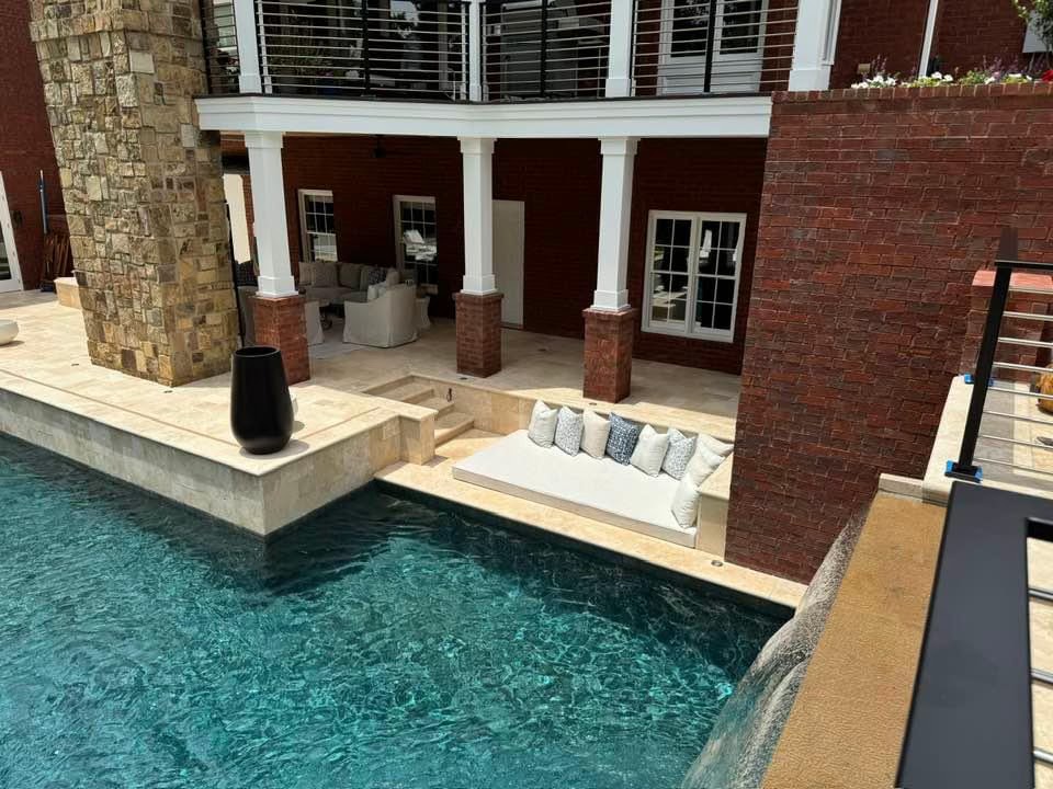 Luxury poolside seating area with built-in lounge and covered patio attached to a brick home